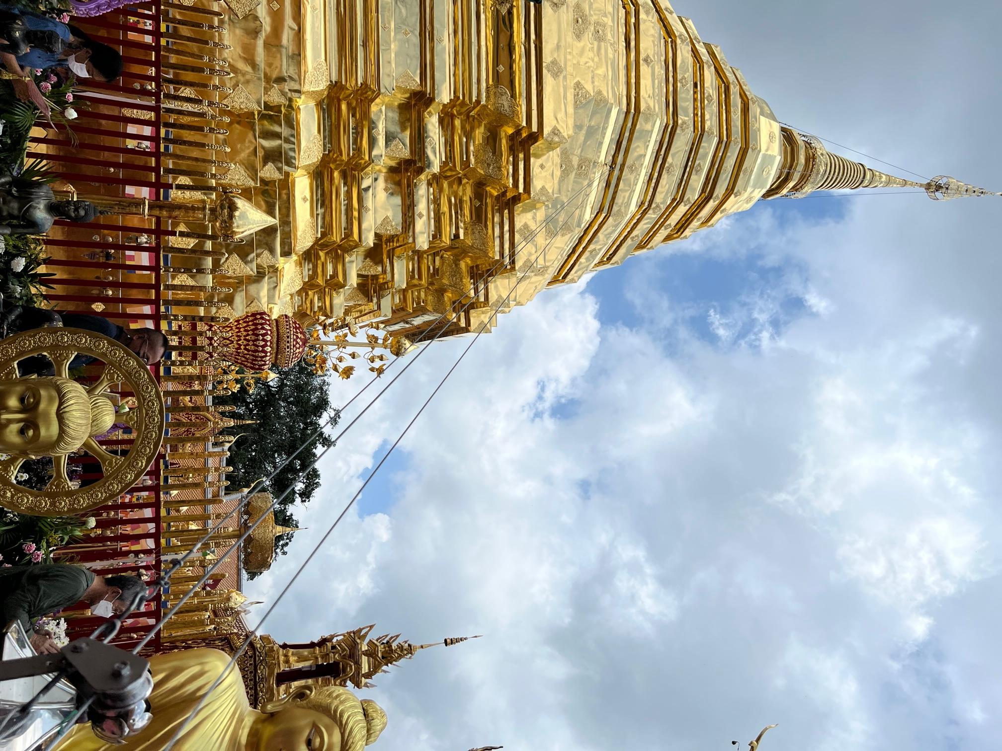 A golden and heavily ornate temple with statues of Buddha in the foreground