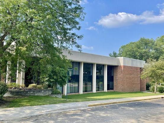 A short brick building with white columns and a light wash stone roof.