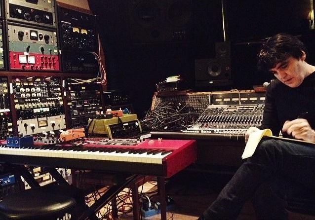 Man writing in room with sound equipment surrounding him